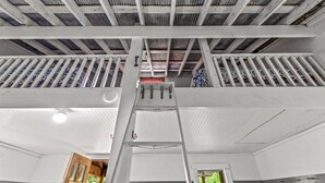 Un plafond haut avec des poutres apparentes et une échelle menant à une mezzanine.
