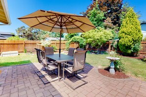 Une terrasse avec une table et des chaises, un parasol et un abreuvoir pour les oiseaux.