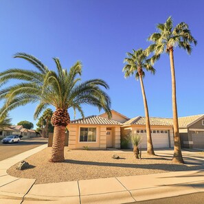 A residential house with a tiled roof, palm trees, and a driveway.