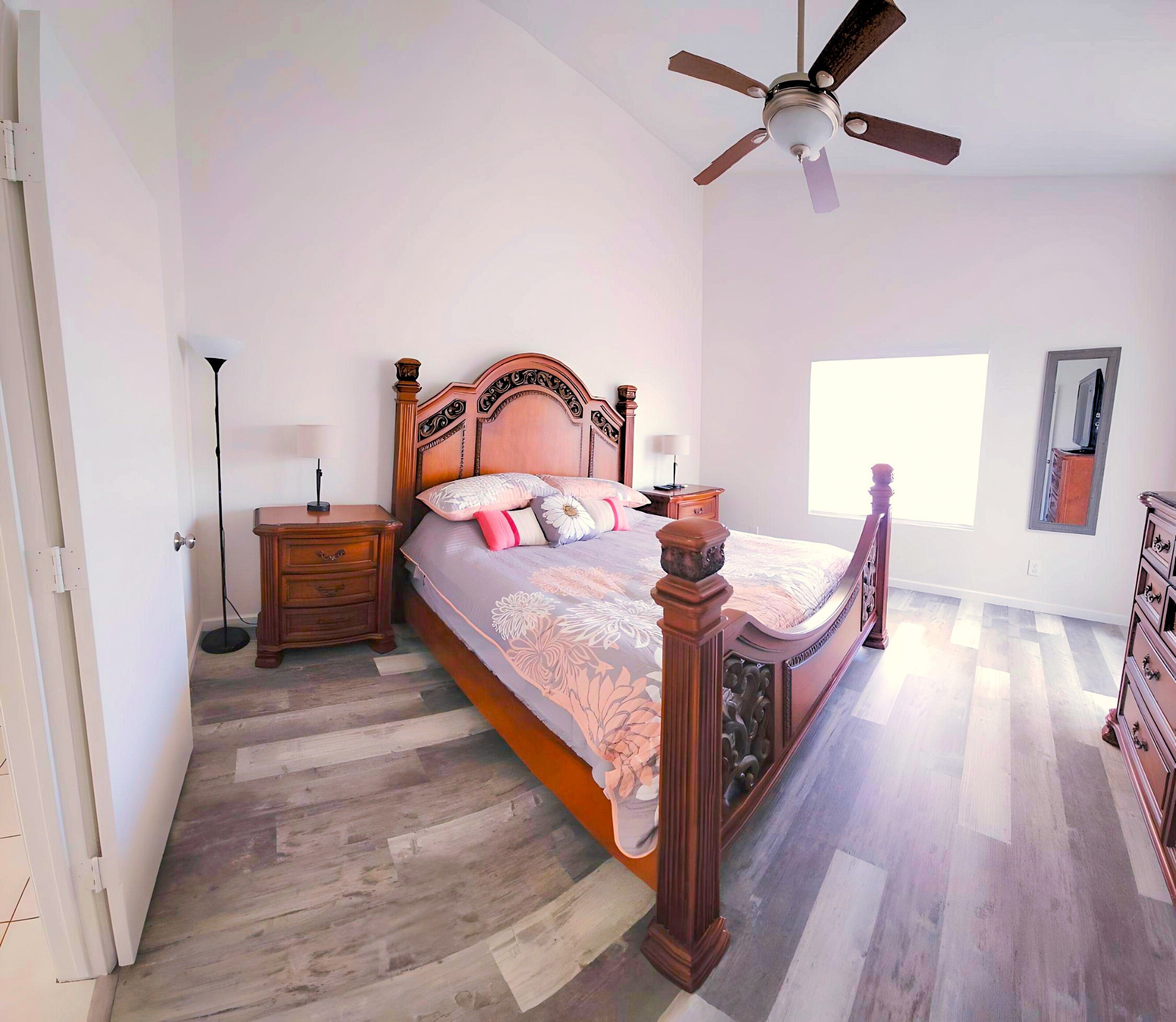 Quarto com cama de madeira, mesa de cabeceira, abajur, ventilador de teto e cômoda.