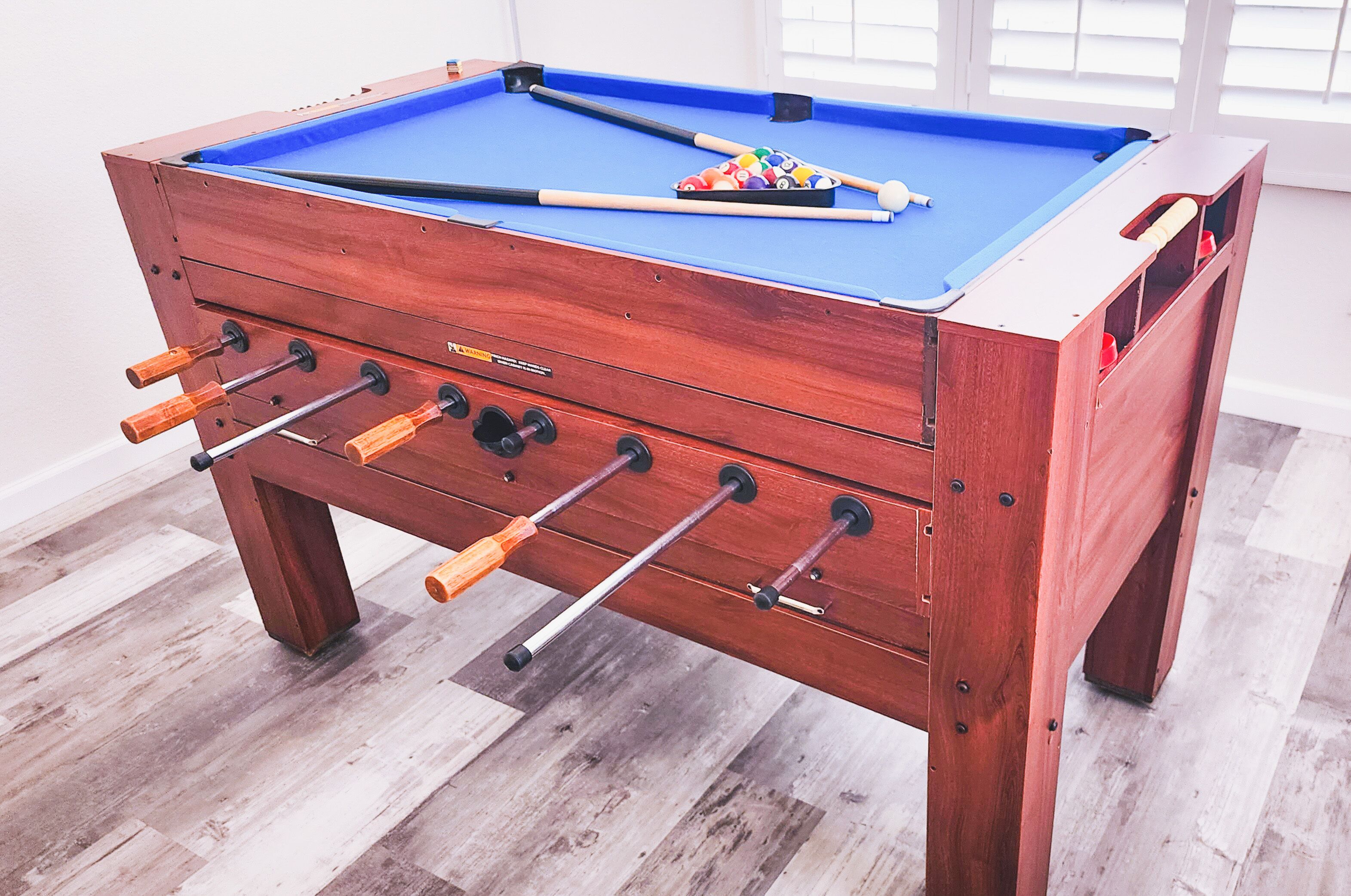 Une table de baby-foot en bois, dotée d’un plateau de jeu bleu et de plusieurs tiges avec des poignées.