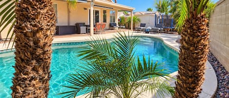 A swimming pool with palm trees, a covered patio, and a building with outdoor seating.