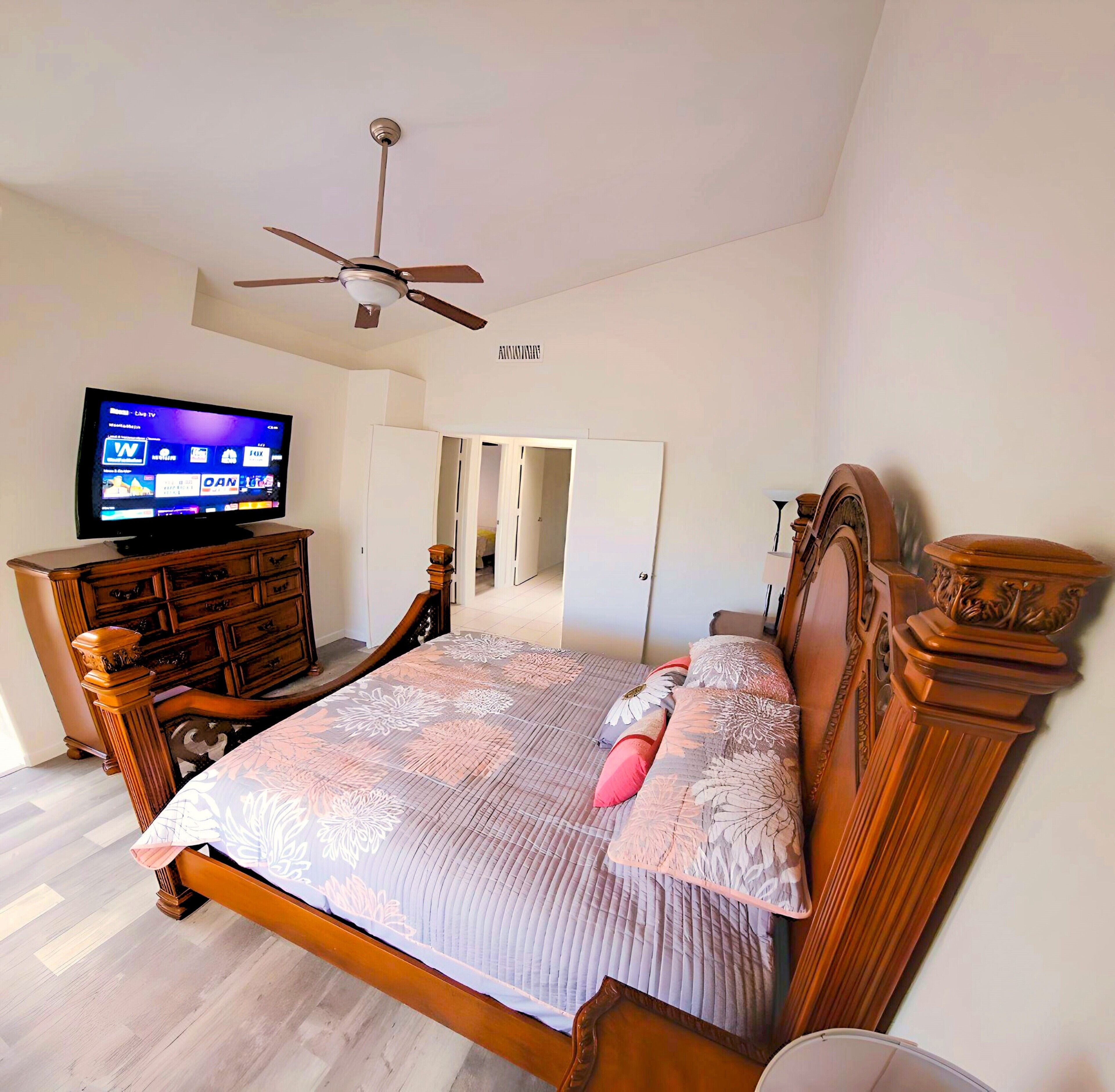 Un dormitorio con cama de madera, televisor, ventilador de techo y armario.