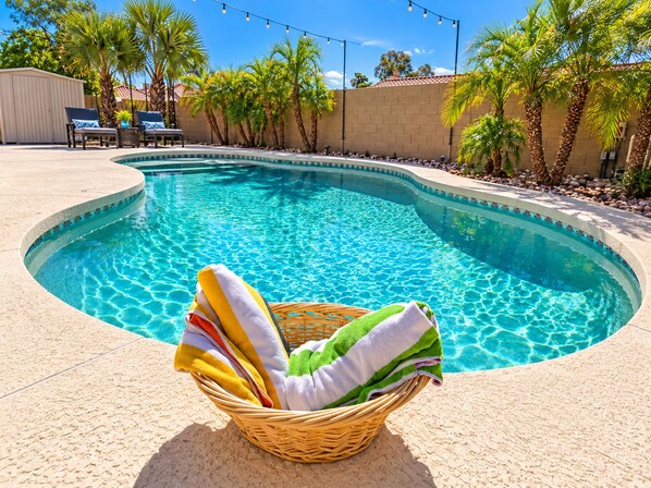 A swimming pool with a curved edge, surrounded by palm trees and a clear blue sky.