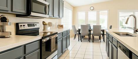 A modern kitchen with grey cabinets, a built-in oven, and a dining area with a table and chairs.