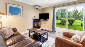Una sala de estar con chimenea, sofás de cuero, una mesa de centro, un televisor de pantalla plana y un amplio ventanal corredera que da a un jardín.