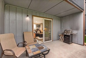 Un patio techado con una parrilla, sillas y vista hacia la casa.