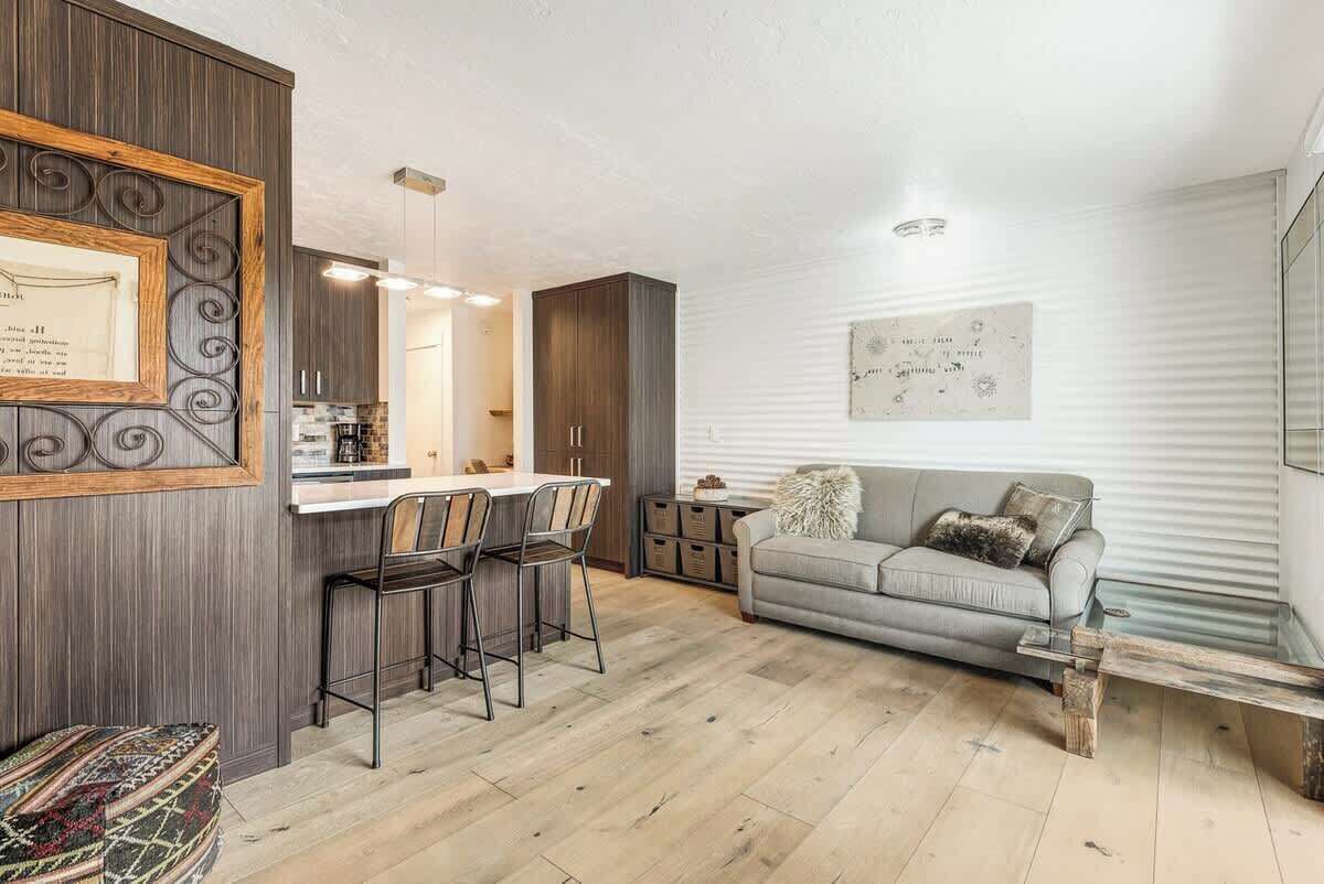 A modern living room with a grey sofa, a wooden coffee table, and a dining area with a kitchen in the background.
