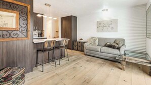Una sala de estar moderna con un sofá gris, una mesa de centro de madera y un comedor con una cocina al fondo.