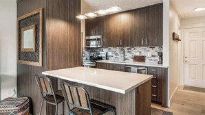 Una cocina moderna con armarios de madera oscura, una isla central con taburetes y microondas, además de un salpicadero de azulejos.
