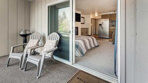 Une pièce dotée d’une porte-fenêtre coulissante donnant sur une cuisine, de deux fauteuils Adirondack et d’un lit avec une literie à rayures.