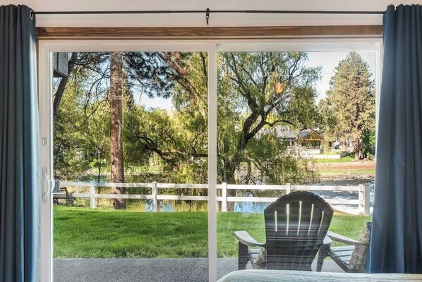 A room with a sliding glass door leading to a grassy area with a white fence and trees.