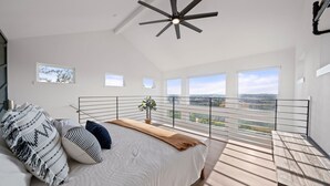 A bedroom with a bed, a ceiling fan, and a balcony with a railing. - Travis Treehouse, Private Couples Getaway  (Austin)