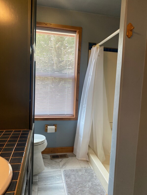 A bathroom with a toilet, a window with blinds, a shower with a curtain, and a tiled floor. - Delightful and secluded 4-bedroom house in Angel Fire perfect for your getaway! (Angel Fire)