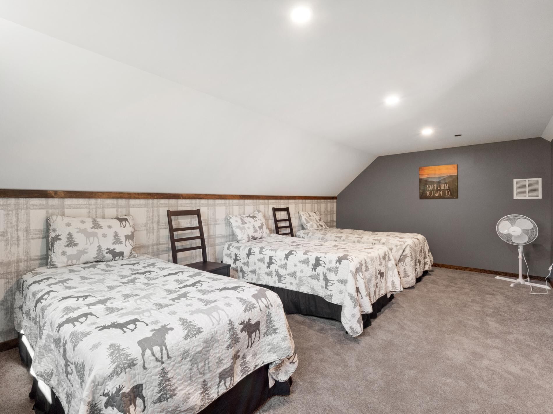 A bedroom with two beds, a standing fan, and a motivational poster on the wall.