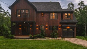 A two-story wooden house with a garage, surrounded by a well-maintained lawn and trees.