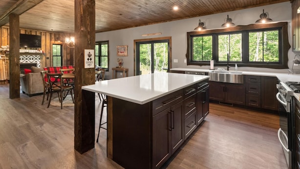 A spacious kitchen with a large island, dark wooden cabinets, and a view of the outdoors through large windows.