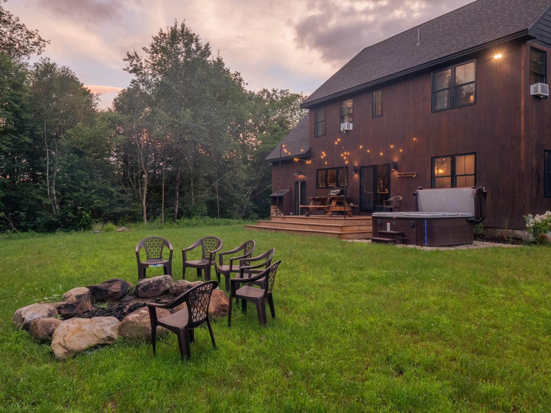 Ein Holzhaus mit einer Terrasse, Sitzgelegenheiten im Freien und einem Whirlpool.