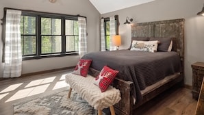 A bedroom with a large bed, a wooden headboard, a window with curtains, a lamp, and a deer head decoration on the wall.