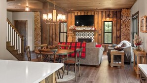 A rustic interior with a wooden ceiling, a fireplace, a dining area, and a living room with a sofa and chairs.