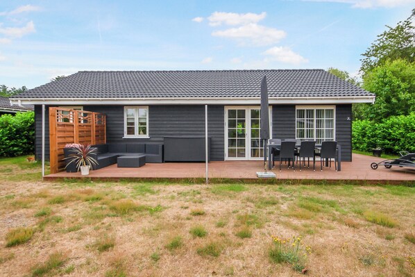 Ein Haus mit dunkler Fassade, einer überdachten Terrasse mit Gartenmöbeln und einem kleinen Garten.