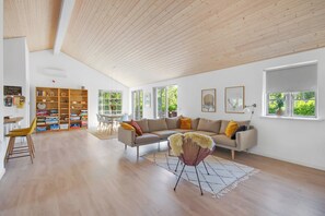 Un salon spacieux avec un plafond en bois, un canapé, un fauteuil, une bibliothèque et un coin repas.