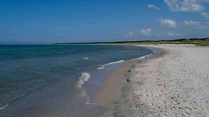 A beach with clear blue water, sandy shore, and a distant horizon.