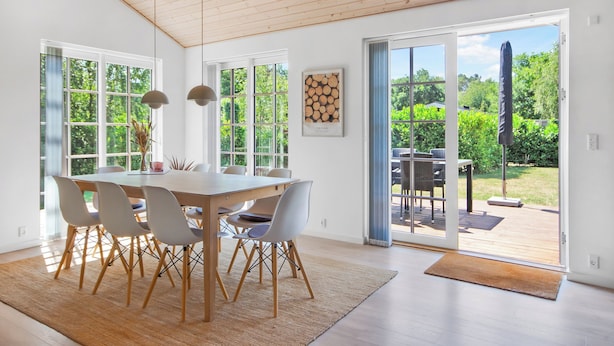 A dining area with a wooden table and chairs, large windows, and a view of the outdoors.