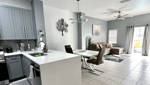 A modern kitchen with grey cabinets, a central island, and a dining area with a sofa and chairs.