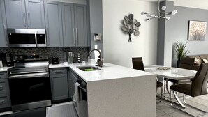 A modern kitchen with grey cabinets, stainless steel appliances, a central island, and a dining area with a chandelier.