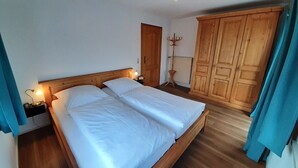 A bedroom with a wooden bed, a nightstand with a lamp, a wardrobe, and a door. - Steinplatte vacation apartment, 3-star with 45 sqm, home, balcony (Gstadt am Chiemsee)