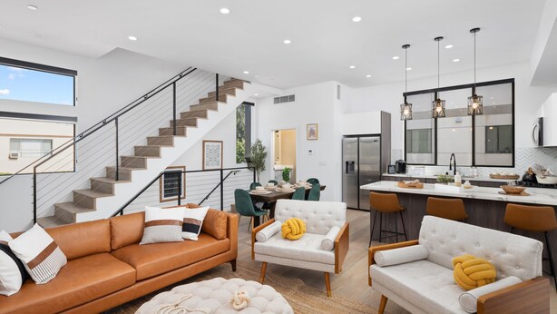 A modern living room with a staircase, a dining area, and a kitchen with bar seating.