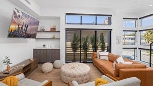 A modern living room with a sofa, ottoman, and a flat-screen TV mounted on the wall.