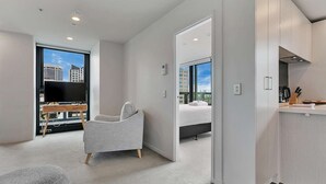 A modern hotel room with a large bed, a seating area with a TV, and a view of the cityscape.