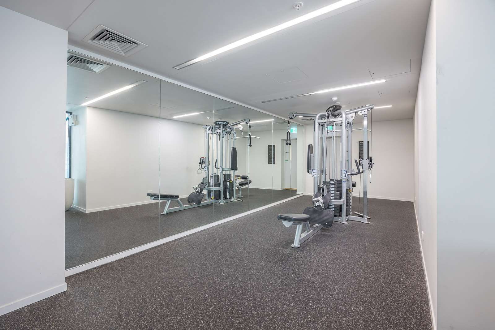 Ein Fitnessraum mit Spiegelwänden, Trainingsgeräten und Teppichboden.
