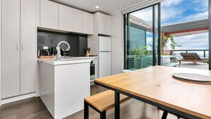 A modern kitchen with white cabinetry, a wooden island, and a large window overlooking a balcony with outdoor seating.