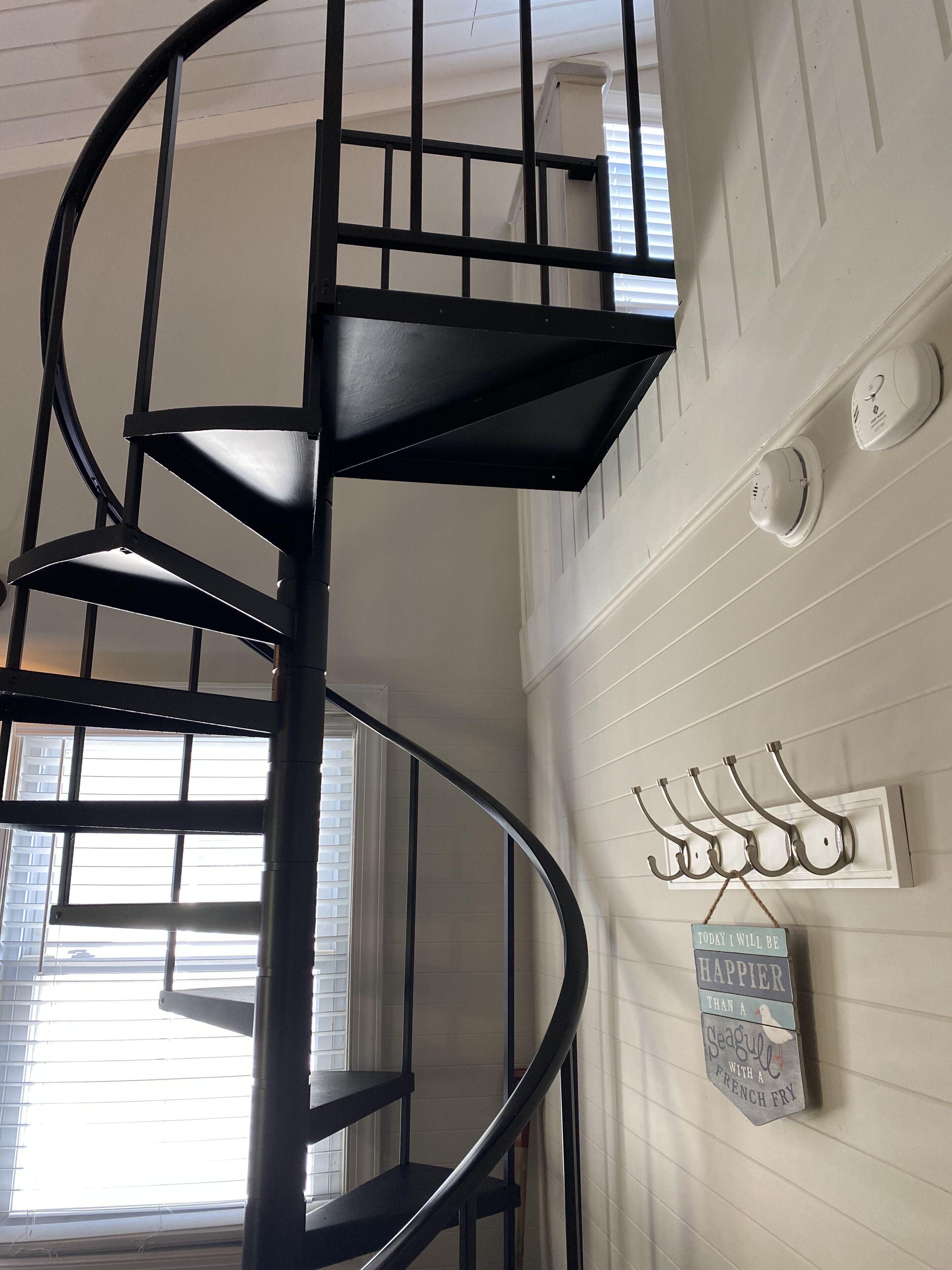 A spiral staircase with a metal railing, a wall-mounted smoke detector, and a decorative sign with a bird and text.
