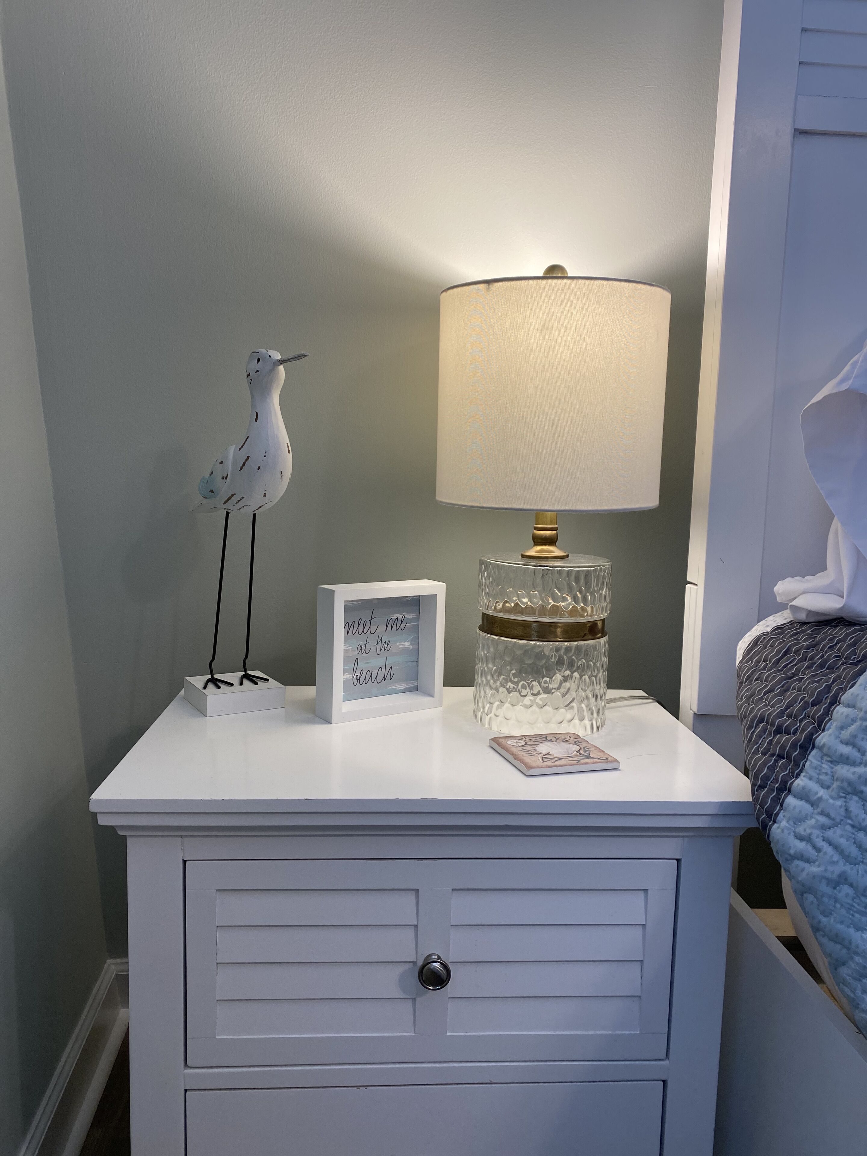 A white bedside table with a lamp, a framed photo, and a decorative seagull.