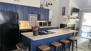 A modern kitchen with blue cabinetry, a black refrigerator, a microwave, and a central island with stools. - Blessed Rest (Edisto Island)