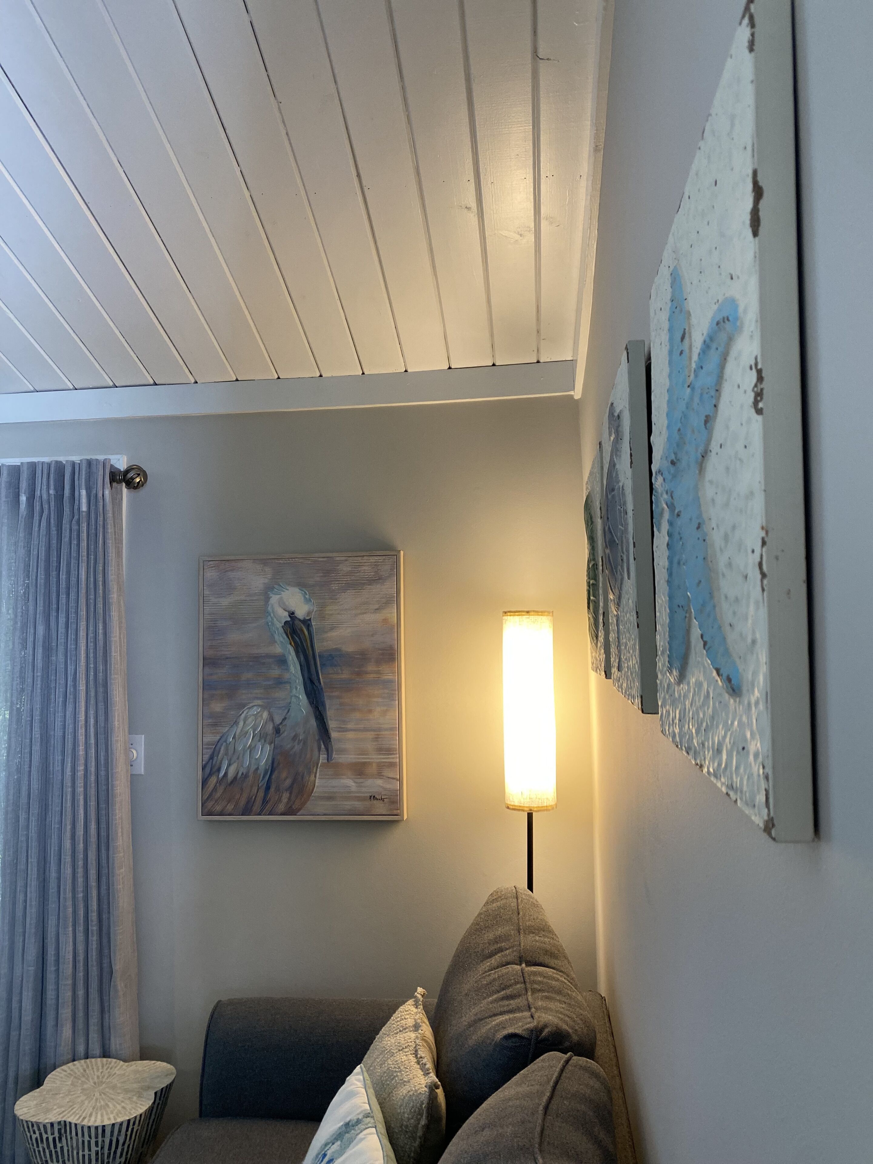 A living room with a gray sofa, a painting of a bird, a lamp, and a textured wall art piece.