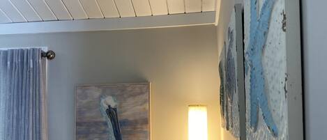 A living room with a gray sofa, a painting of a bird, a lamp, and a textured wall art piece.