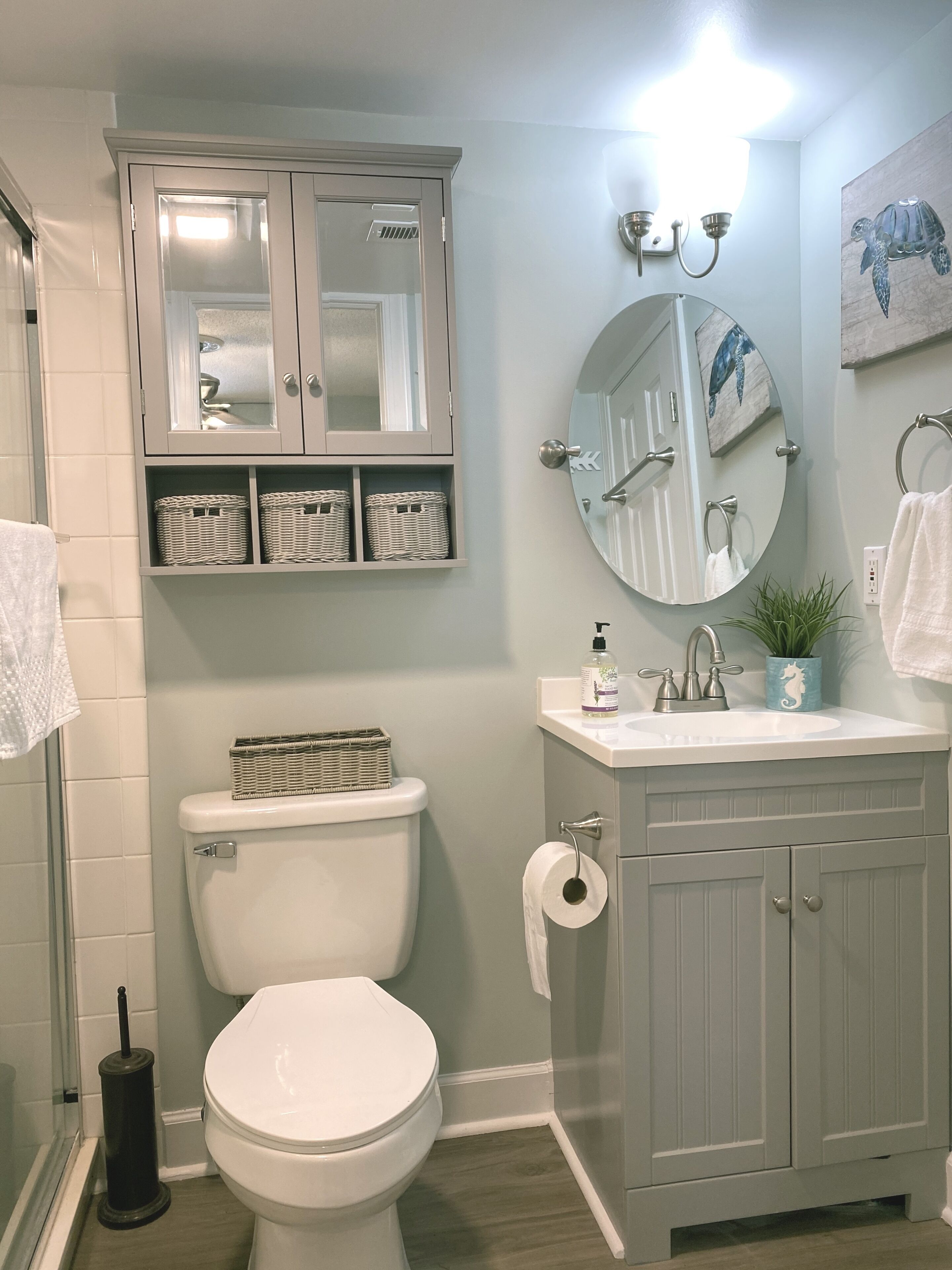 A bathroom with a toilet, a sink, a mirror, and a cabinet with baskets.