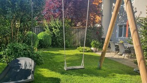 A backyard with a swing set, a dining area with chairs, and a wooden fence. - Ferienwohnung 54qm mit Sep. Schlafzimmer und Terrasse (Prien am Chiemsee)