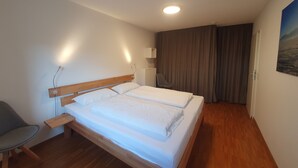 A hotel room with a wooden bed, a desk, a chair, a nightstand, and a painting on the wall. - Ferienwohnung 54qm mit Sep. Schlafzimmer und Terrasse (Prien am Chiemsee)