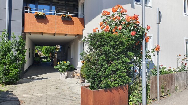 A building entrance with a covered walkway, potted plants, and a metal fence. - Ferienwohnung 54qm mit Sep. Schlafzimmer und Terrasse (Prien am Chiemsee)