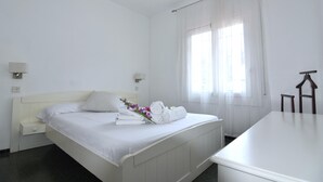 A clean, white hotel room with a bed, bedside tables, a desk, and a window with curtains. - Rental in La Almadrava beach, Roses. Apartment with sea views, private terrace, equipped kitchen. Book now! (Roses)