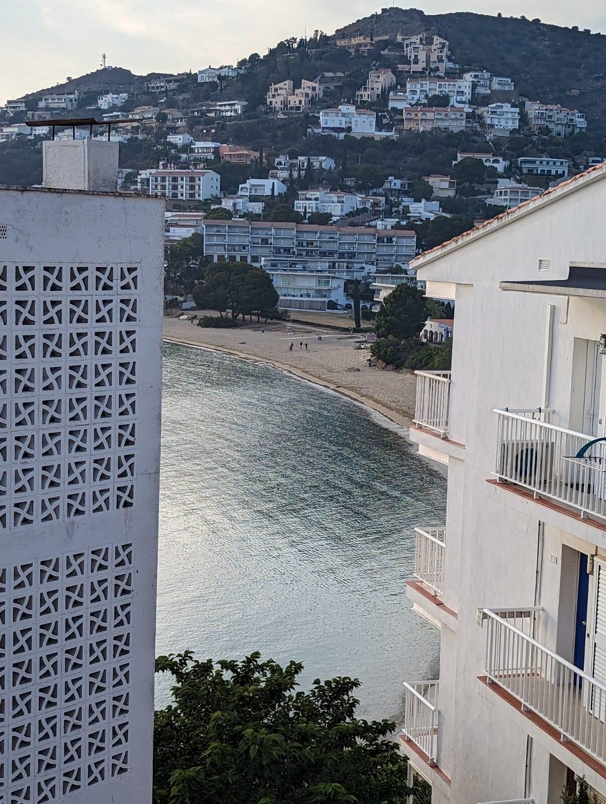A coastal view with buildings on a hillside, a beach, and a body of water.