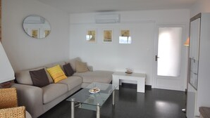 A modern living room with a glass coffee table, a beige sofa with cushions, a small white side table, and a door leading to another room. - Rental in La Almadrava beach, Roses. Apartment with sea views, private terrace, equipped kitchen. Book now! (Roses)