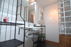 Een badkamer met een wit wastafel, een spiegel, een douche en een raam met gezandstraald glas.