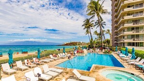 A hotel pool area with lounge chairs, a hot tub, and palm trees.